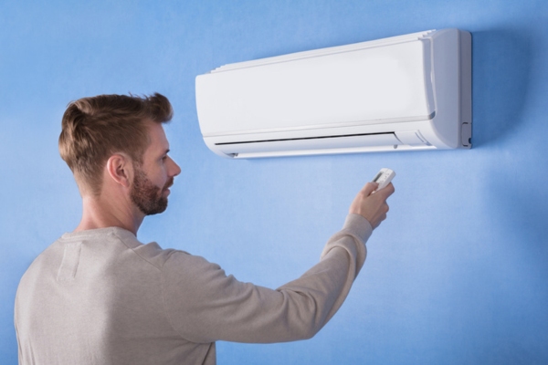 man turning off ductless AC using remote