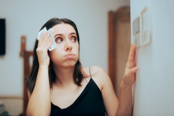 woman sweating checking home AC thermostat