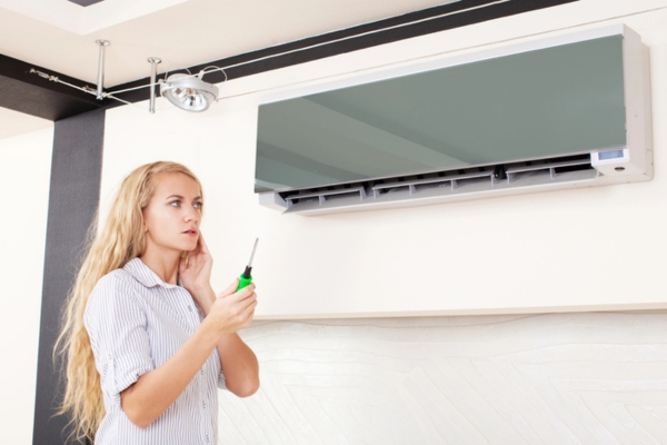 woman looking at broken air conditioner clueless with a screw driver on hand