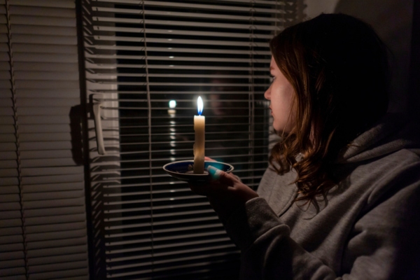 woman looking through the window with a candle due to power surge