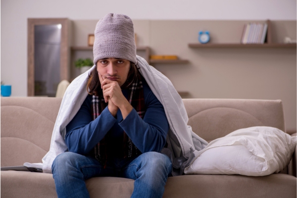 man feeling extra cold indoors wearing a beanie and a blanket depicting incorrect furnace size